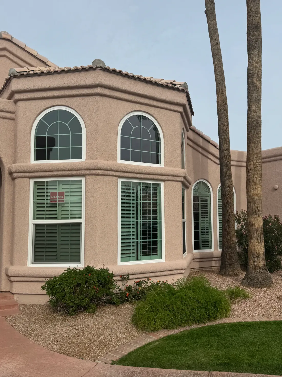 Bay of arched windows on a blush stucco house, the stucco cut in tight to new white window frames with a bullnose band course running under the sills.
