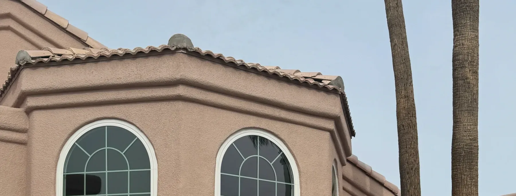 Bay of arched windows on a blush stucco house, the stucco cut in tight to new white window frames with a bullnose band course running under the sills.