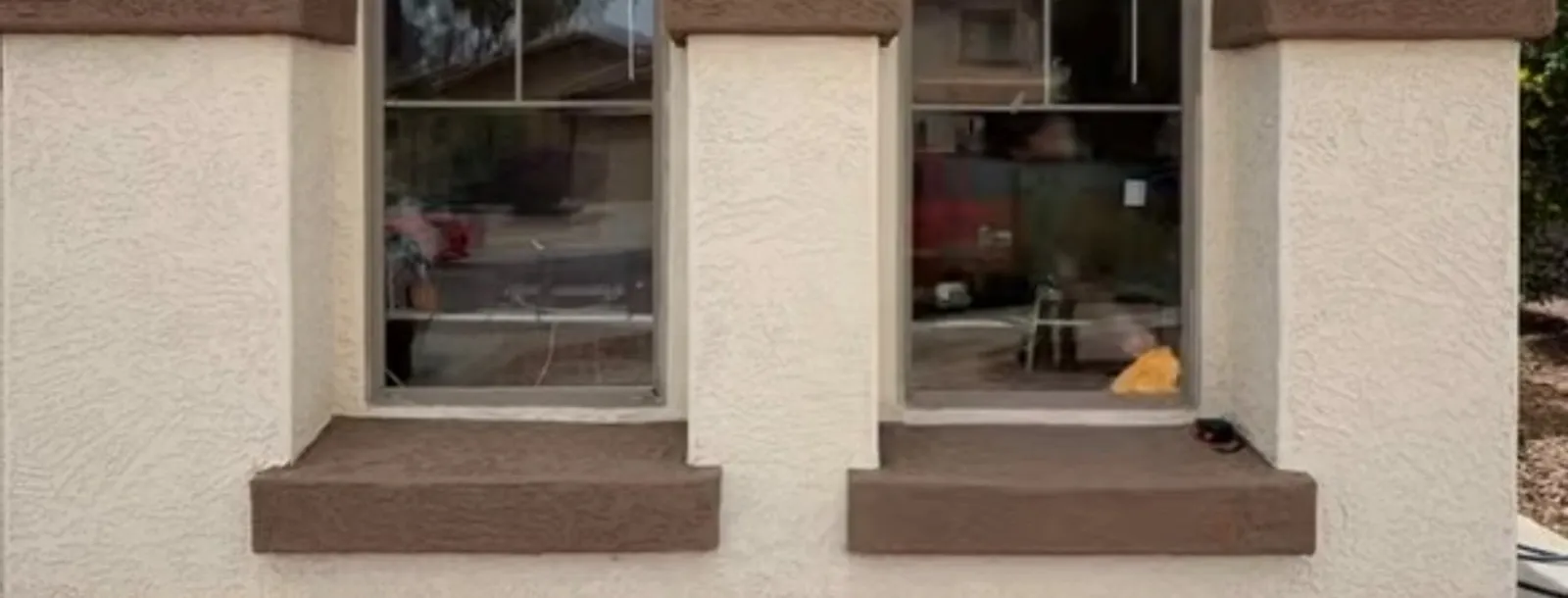 Two arched window openings in a cream stucco wall with brown foam-and-stucco sills and a band course carried across between them.