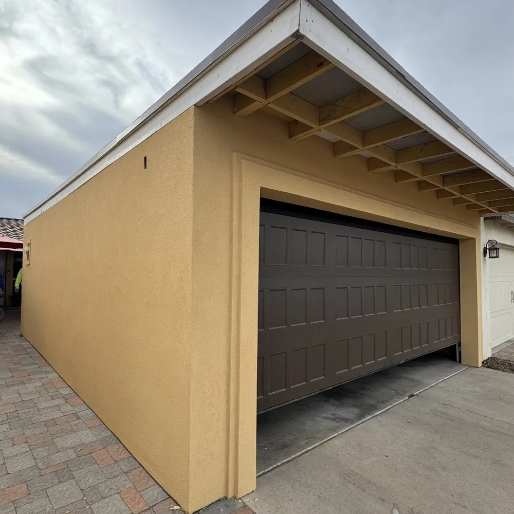 Newly stuccoed and painted garage addition in mustard gold, the stucco run clean into the door surround and up to the exposed rafter tails.