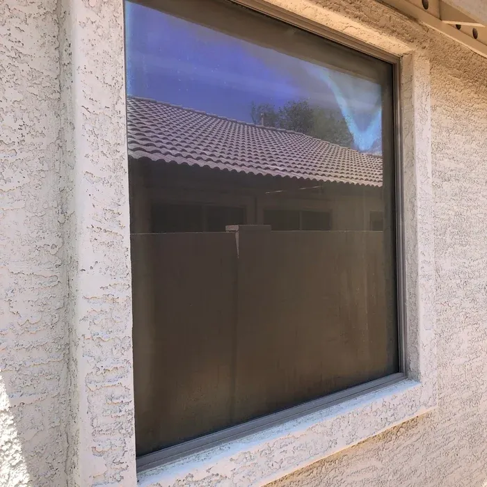 Heavy white lace-texture stucco around a window, the return edge chipped and weathered where the finish has broken away from the frame.