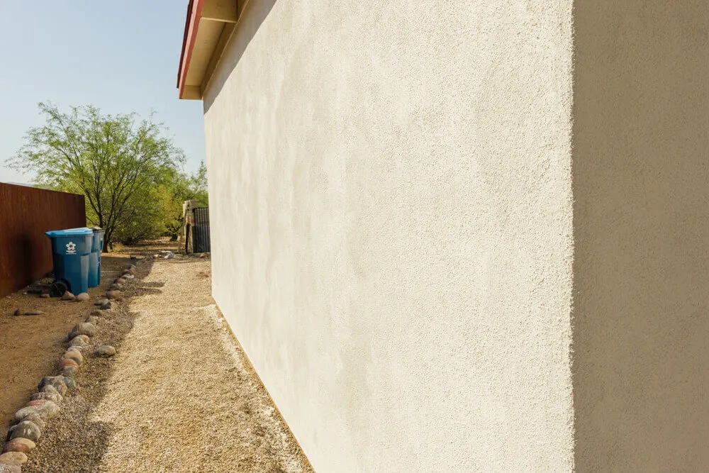 Long white sand-finish stucco wall running away in perspective under full sun, the fine even grain of the float finish catching the light.