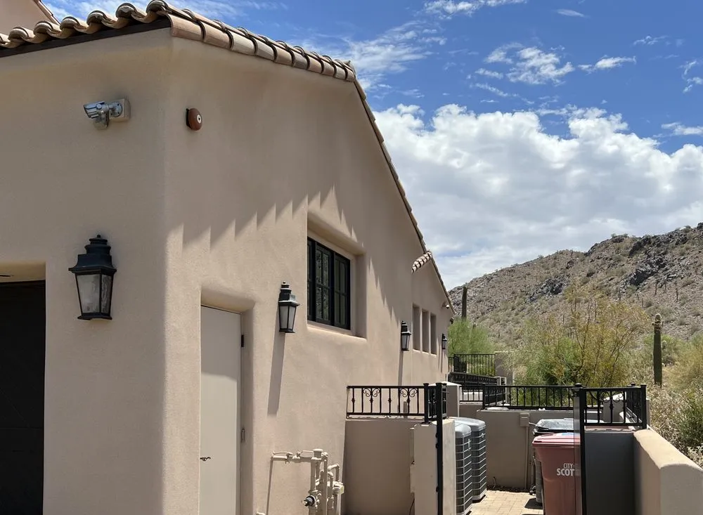 Side yard of a single-storey Scottsdale home, low sun raking across a smooth cream stucco wall and tile roof with desert hillside behind.