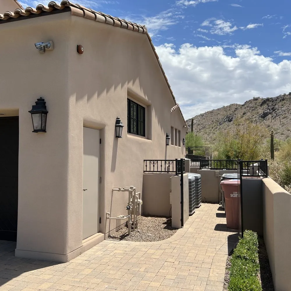 Side yard of a single-storey Scottsdale home, low sun raking across a smooth cream stucco wall and tile roof with desert hillside behind.