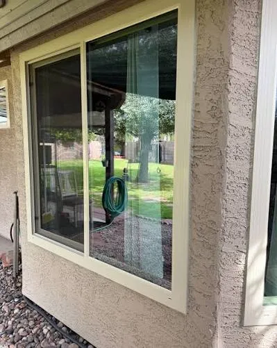 Slider window in a heavily textured stucco wall, cream stucco trim run tight to the frame and sealed along the head and jambs.